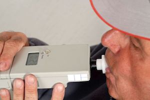 Man undergoing an alcohol test using a breathalyzer.