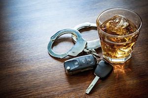 An alcoholic beverage in a glass, handcuffs, and car keys on a table top.