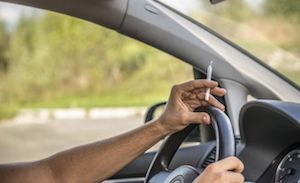 Driver holding marijuana with hands on steering wheel.