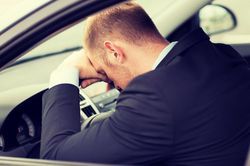 A male driver sleeping with his head on the steering wheel.